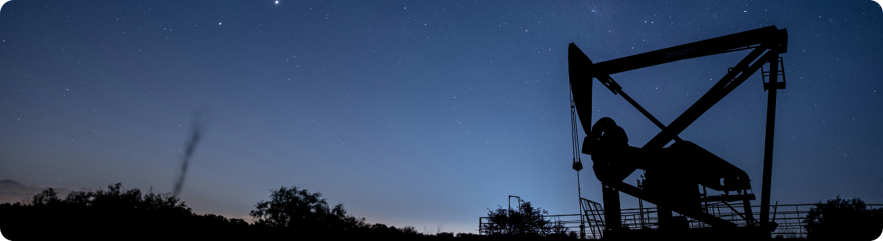 Silhouette of an oil pump jack against a starry twilight sky, with dark scrubland on the horizon.