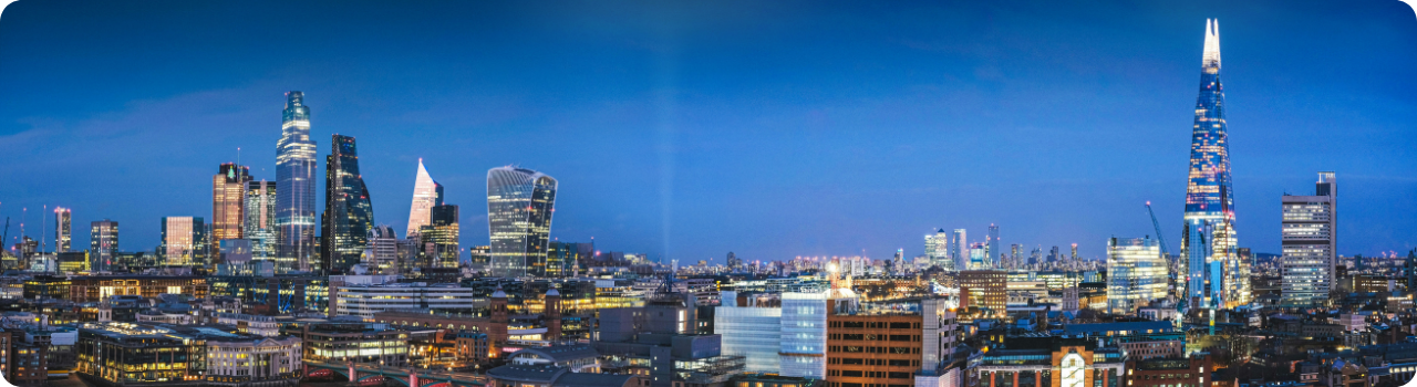 London's financial district skyline lit up at dusk, viewed across the city rooftops.