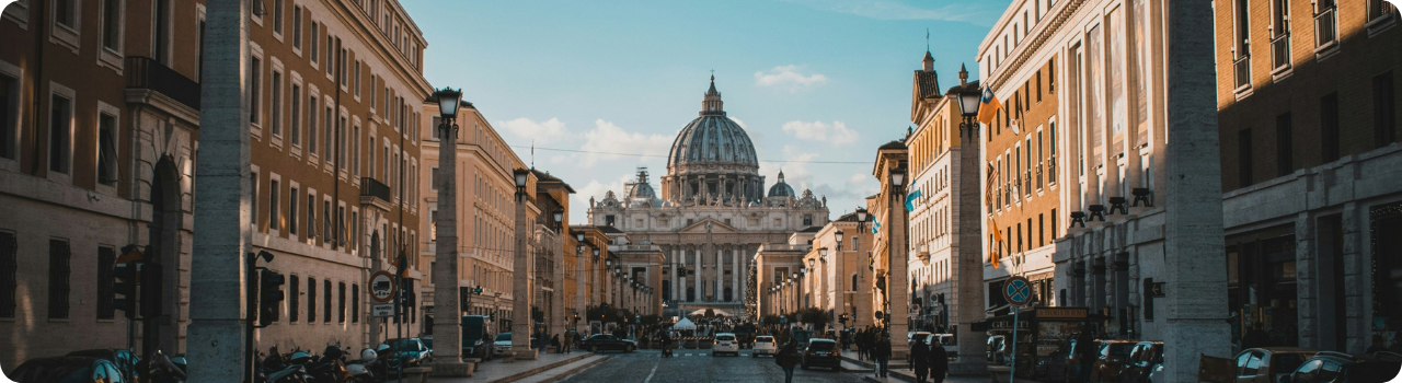View down Via della Conciliazione in Rome towards St Peter's Basilica, its dome lit by late afternoon sun.