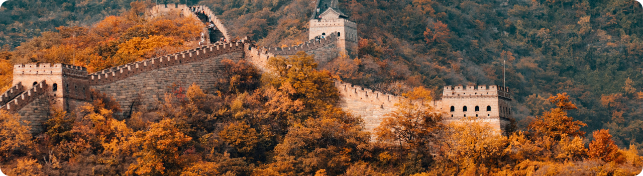 The Great Wall of China winding along a forested ridge in autumn, with watchtowers rising above orange foliage